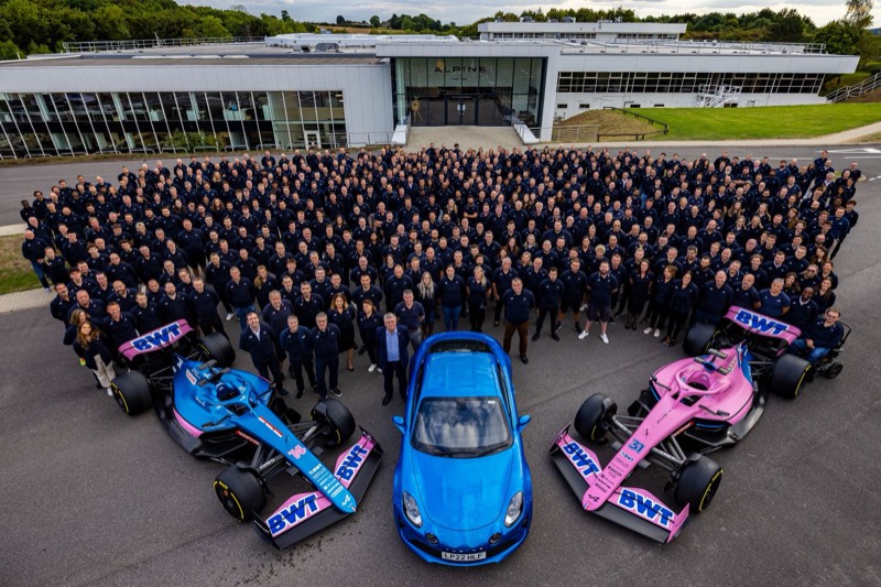 Several hundred Alpine F1 Team staff outside the team’s Enstone factory, with two Formula 1 cars and an Alpine road car.